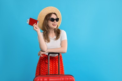 Photo of Happy traveller in sunglasses with suitcase, passport and ticket on light blue background, space for text