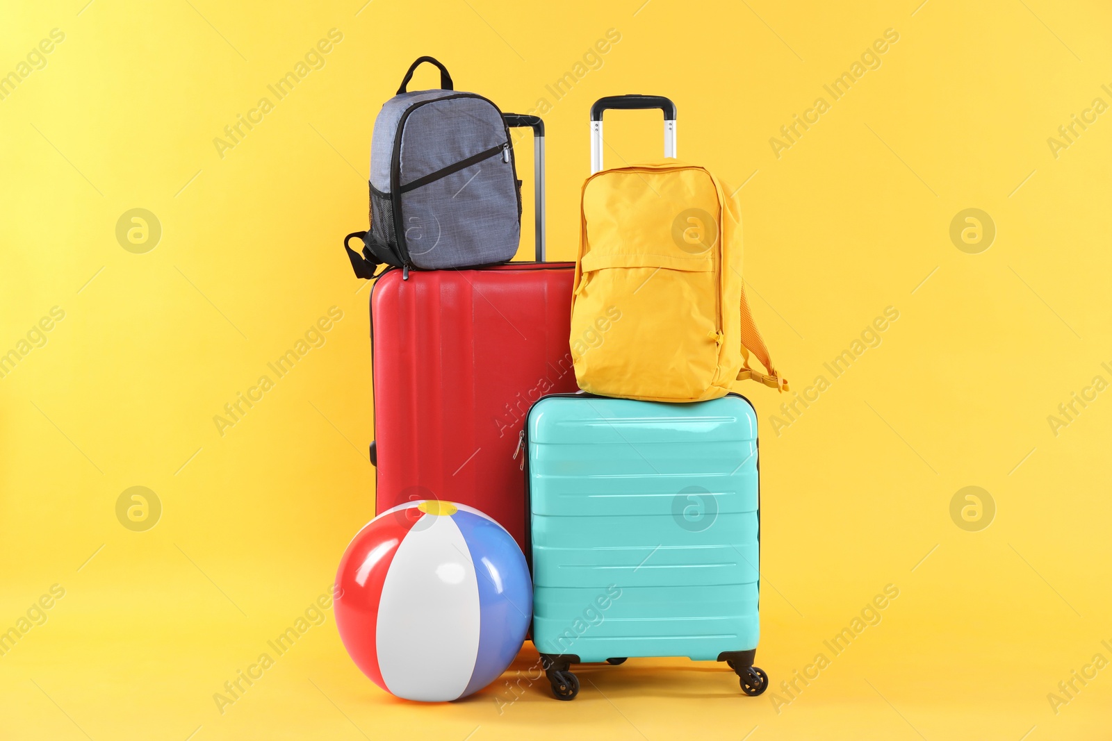 Photo of Travel abroad. Packed suitcases, beach ball and backpacks on yellow background