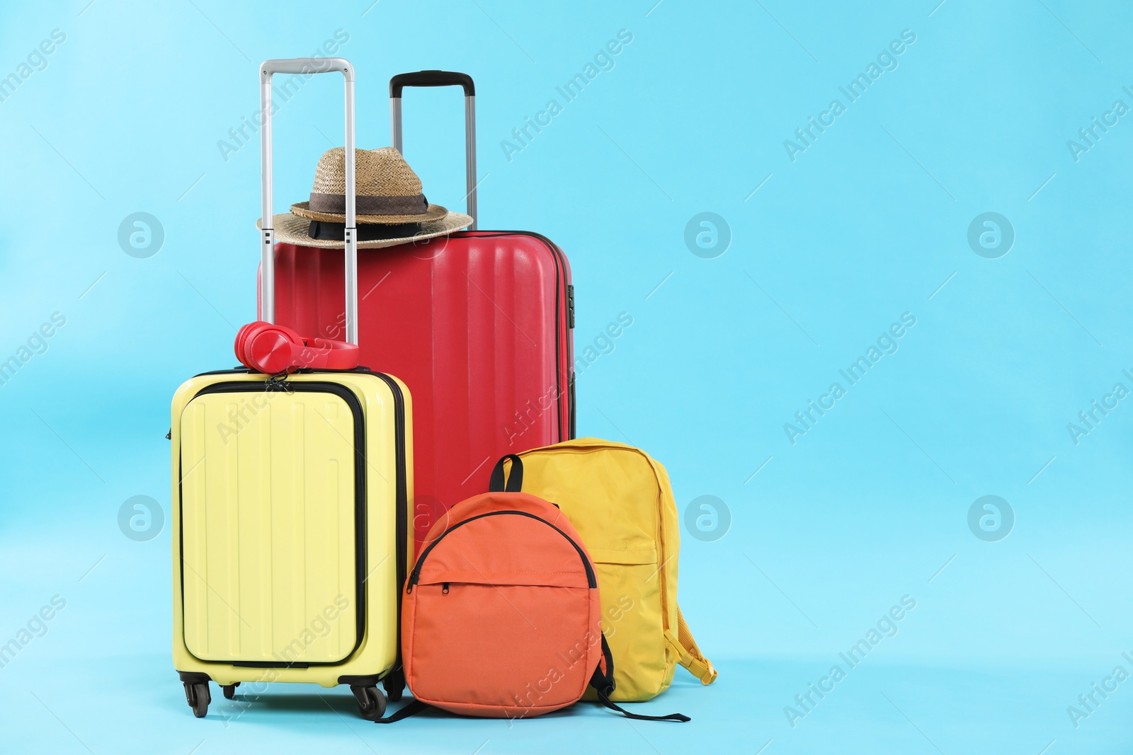 Photo of Travel abroad. Packed suitcases, backpacks, headphones and hats on light blue background. Space for text