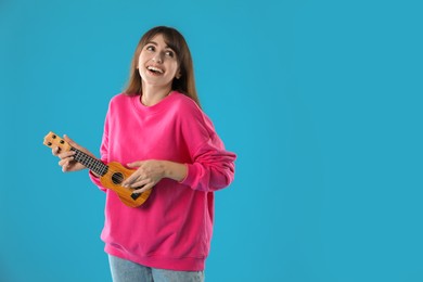 Photo of Happy woman playing ukulele on light blue background, space for text