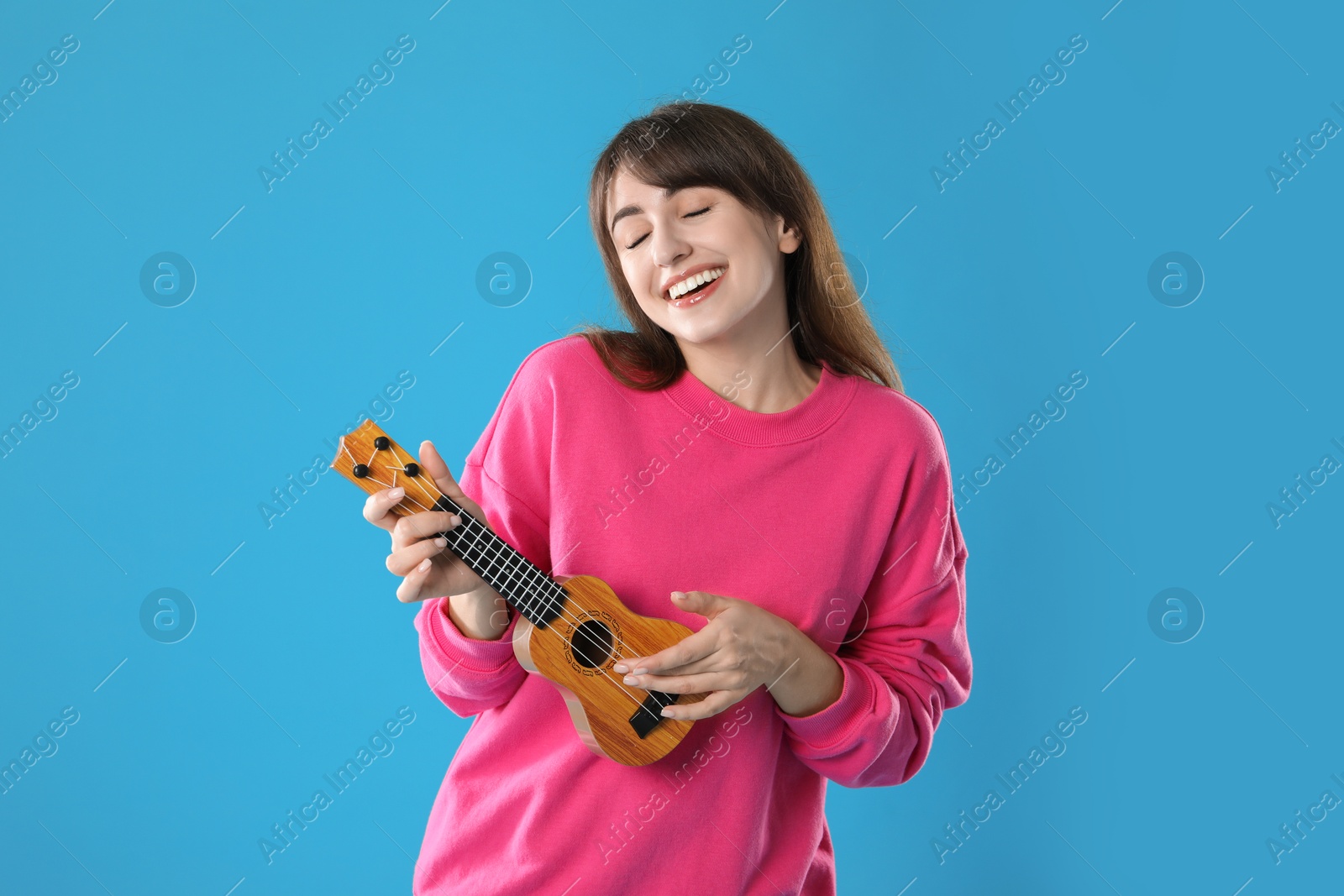 Photo of Happy woman playing ukulele on light blue background