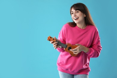 Happy woman playing ukulele on light blue background, space for text