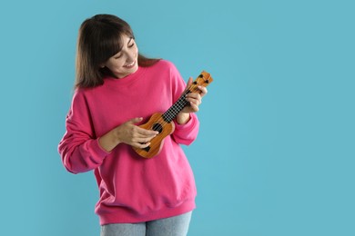 Photo of Happy woman playing ukulele on light blue background, space for text