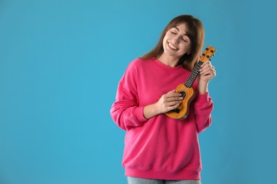 Photo of Happy woman playing ukulele on light blue background, space for text