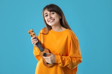 Happy woman playing ukulele on light blue background