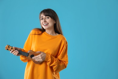 Happy woman playing ukulele on light blue background, space for text