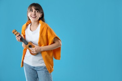 Photo of Happy woman playing ukulele on light blue background, space for text