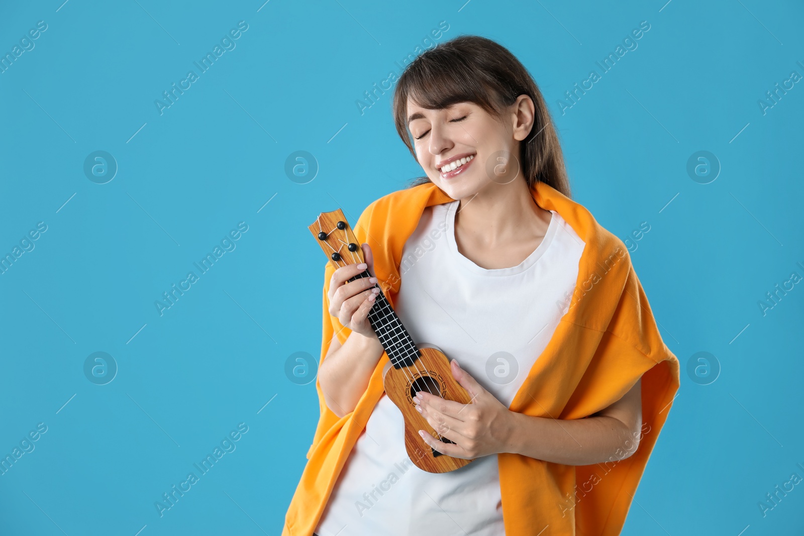 Photo of Happy woman playing ukulele on light blue background, space for text