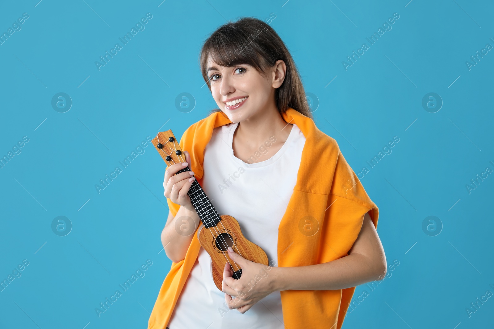 Photo of Happy woman playing ukulele on light blue background