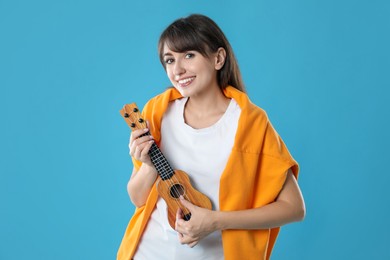 Happy woman playing ukulele on light blue background