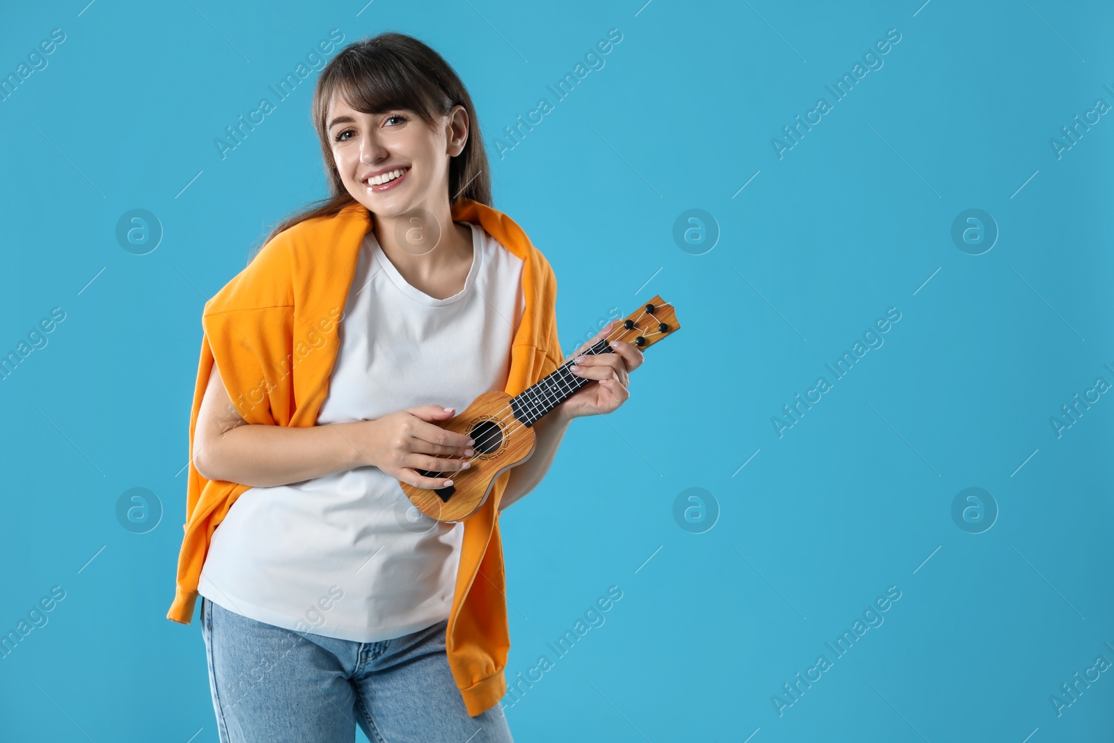 Photo of Happy woman playing ukulele on light blue background, space for text