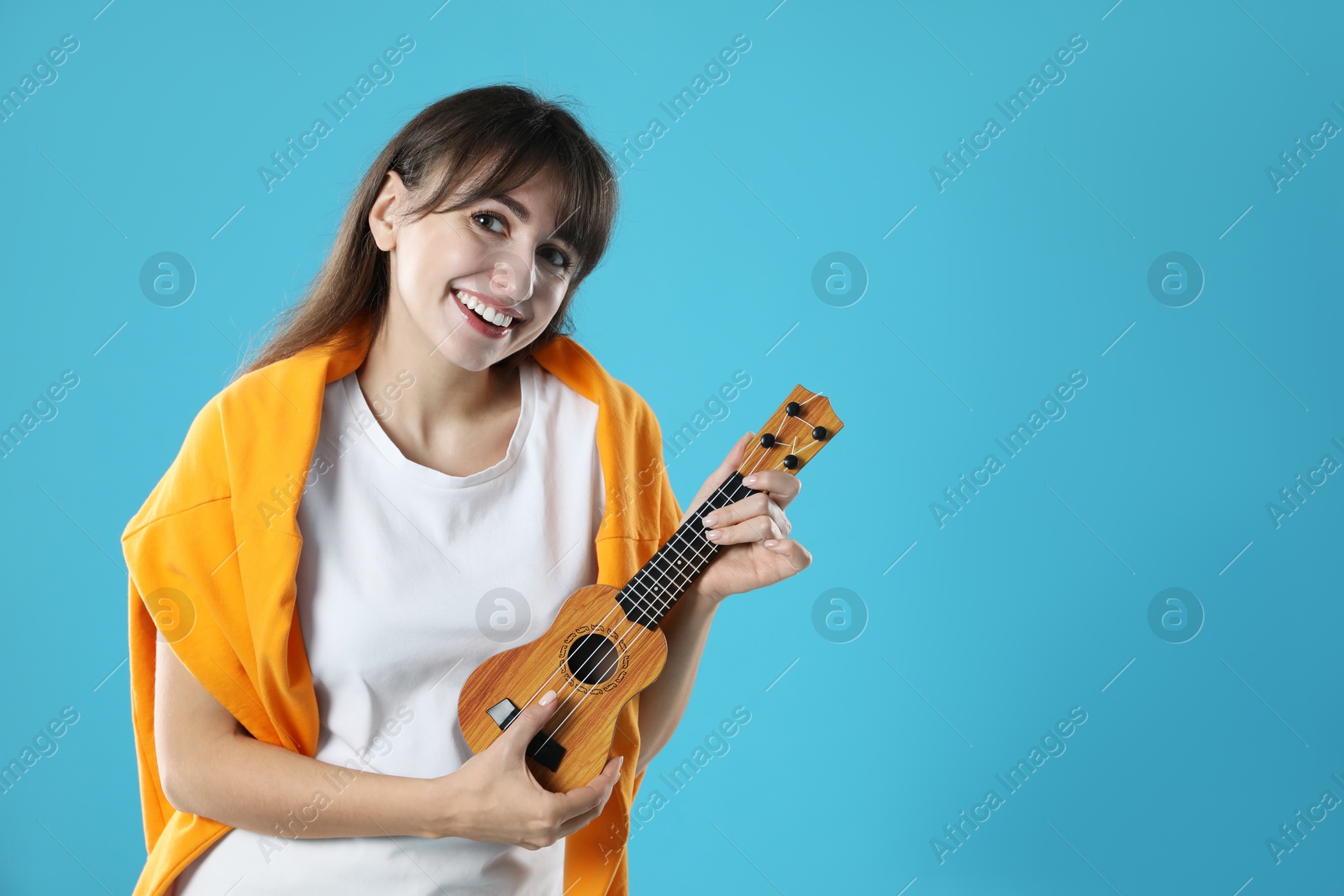 Photo of Happy woman playing ukulele on light blue background, space for text