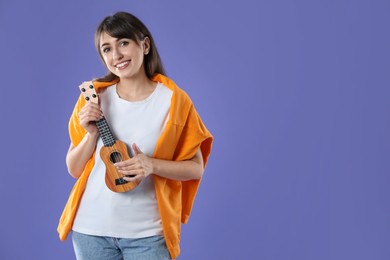 Photo of Happy woman playing ukulele on purple background, space for text