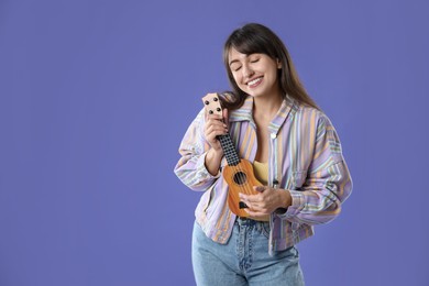 Photo of Happy woman playing ukulele on purple background, space for text