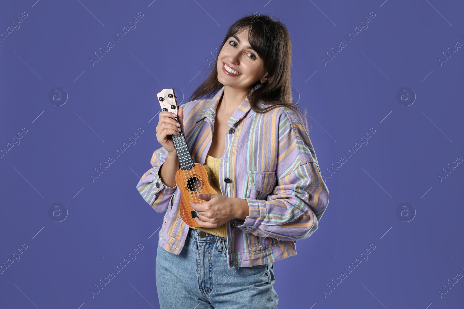 Photo of Happy woman playing ukulele on purple background