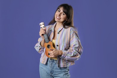 Happy woman playing ukulele on purple background