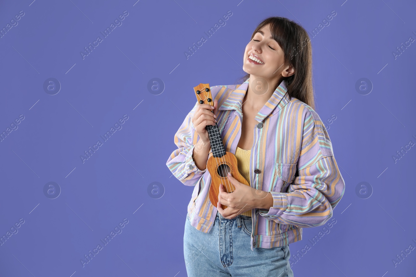 Photo of Happy woman playing ukulele on purple background, space for text