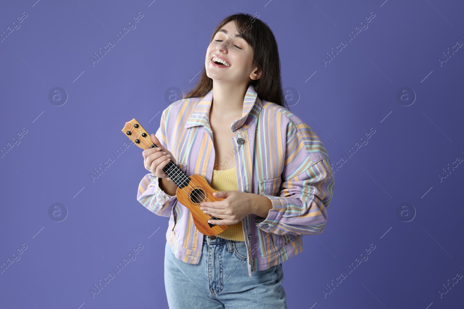 Photo of Happy woman playing ukulele on purple background, space for text