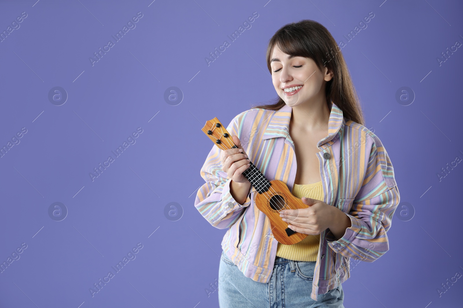 Photo of Happy woman playing ukulele on purple background, space for text