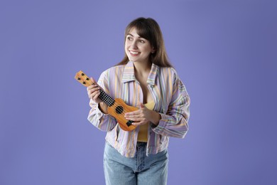 Photo of Happy woman playing ukulele on purple background