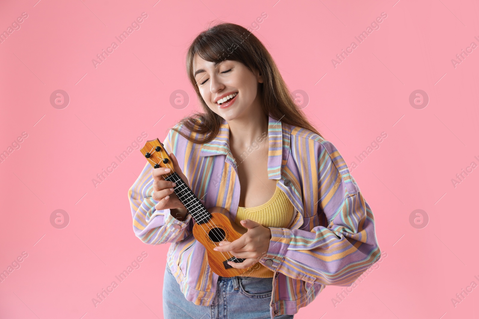 Photo of Happy woman playing ukulele on pink background