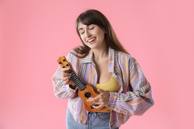 Happy woman playing ukulele on pink background