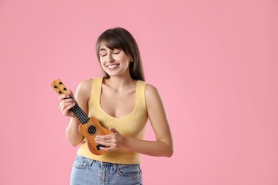 Happy woman playing ukulele on pink background, space for text