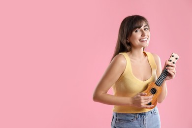 Happy woman playing ukulele on pink background, space for text