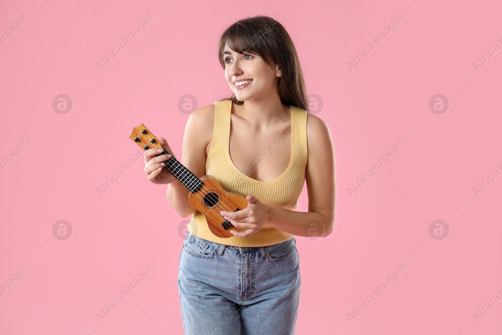 Photo of Happy woman playing ukulele on pink background