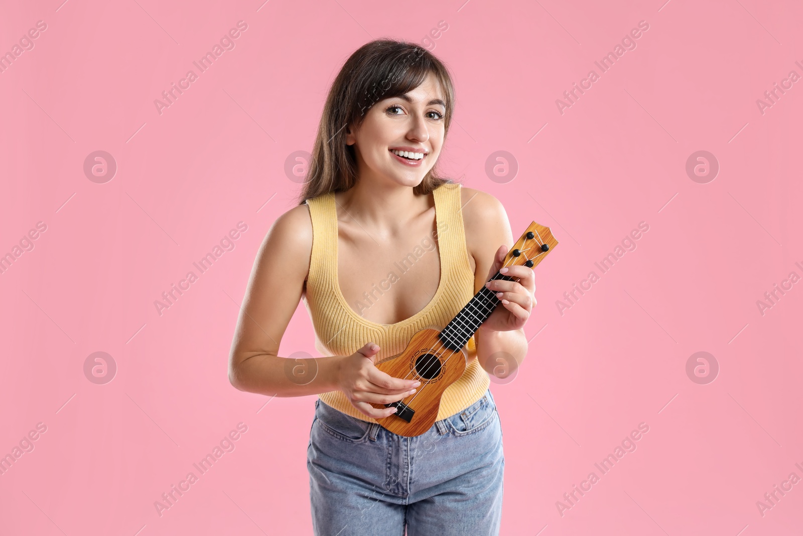 Photo of Happy woman playing ukulele on pink background