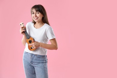 Happy woman playing ukulele on pink background, space for text