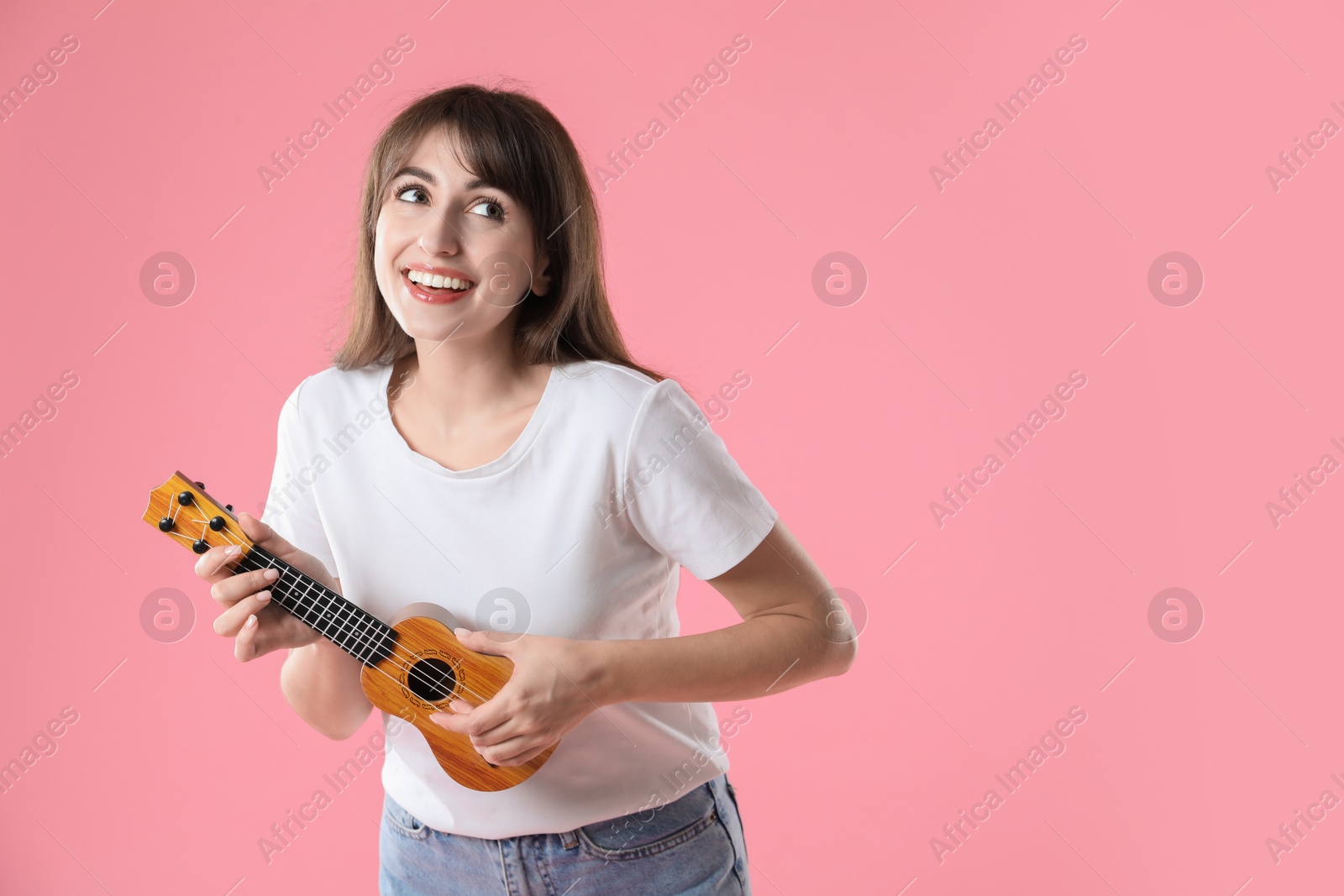 Photo of Happy woman playing ukulele on pink background, space for text