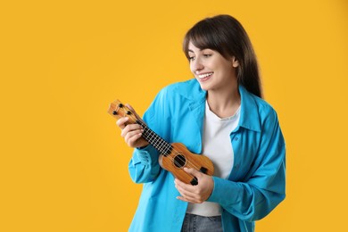 Photo of Happy woman playing ukulele on orange background, space for text