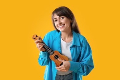 Happy woman playing ukulele on orange background