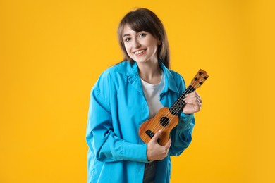 Happy woman playing ukulele on orange background