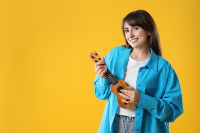 Happy woman playing ukulele on orange background, space for text