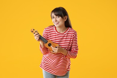 Happy woman playing ukulele on orange background