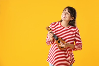 Happy woman playing ukulele on orange background, space for text