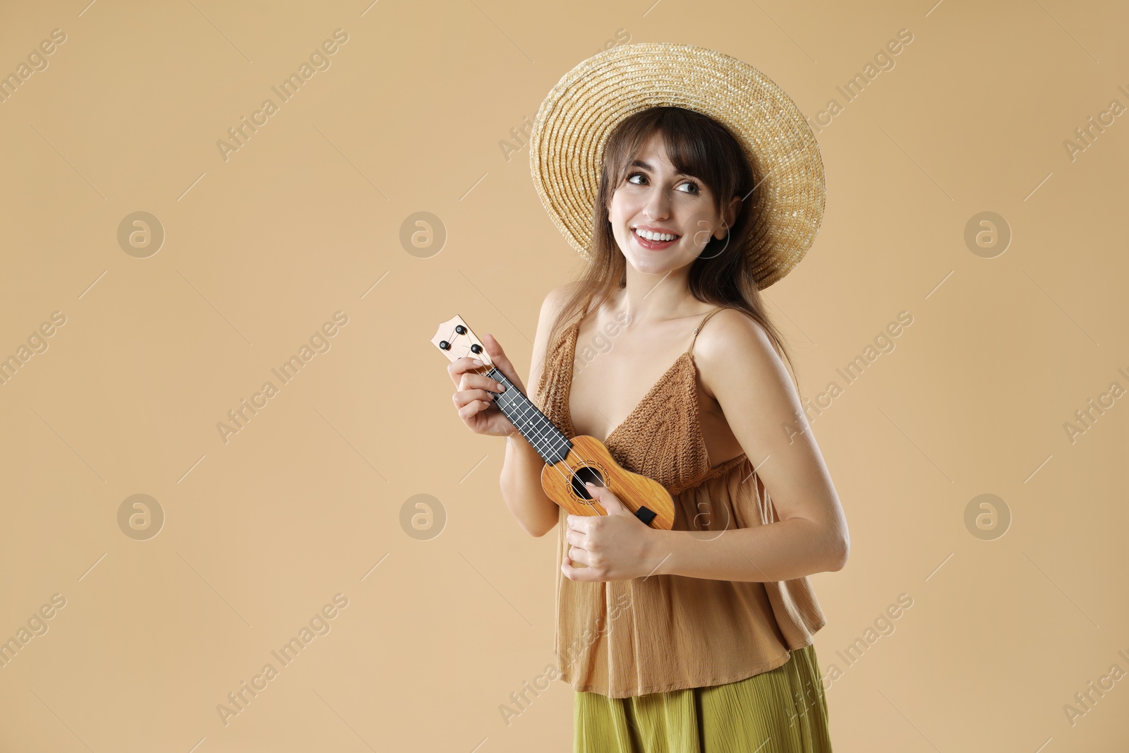 Photo of Happy woman playing ukulele on beige background, space for text