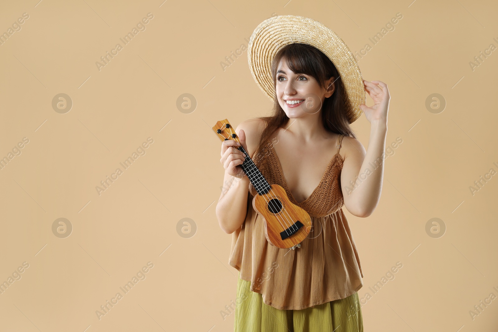 Photo of Happy woman playing ukulele on beige background, space for text