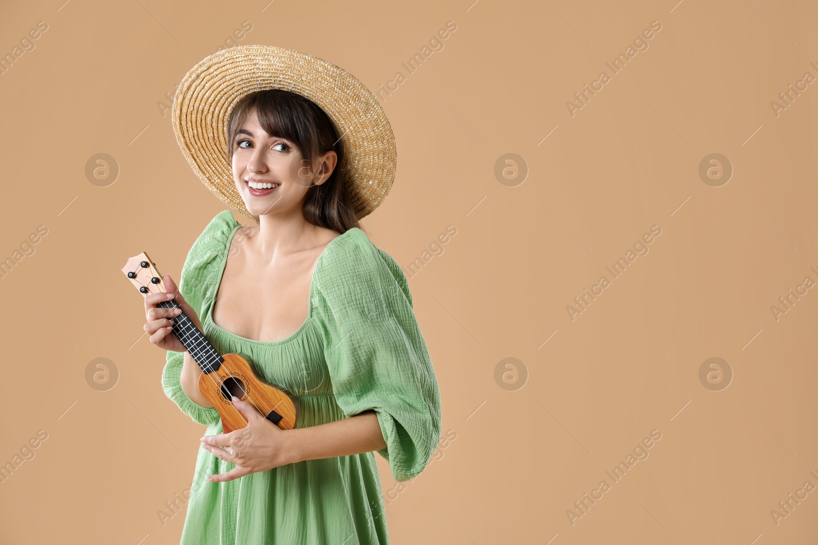 Photo of Happy woman playing ukulele on beige background, space for text