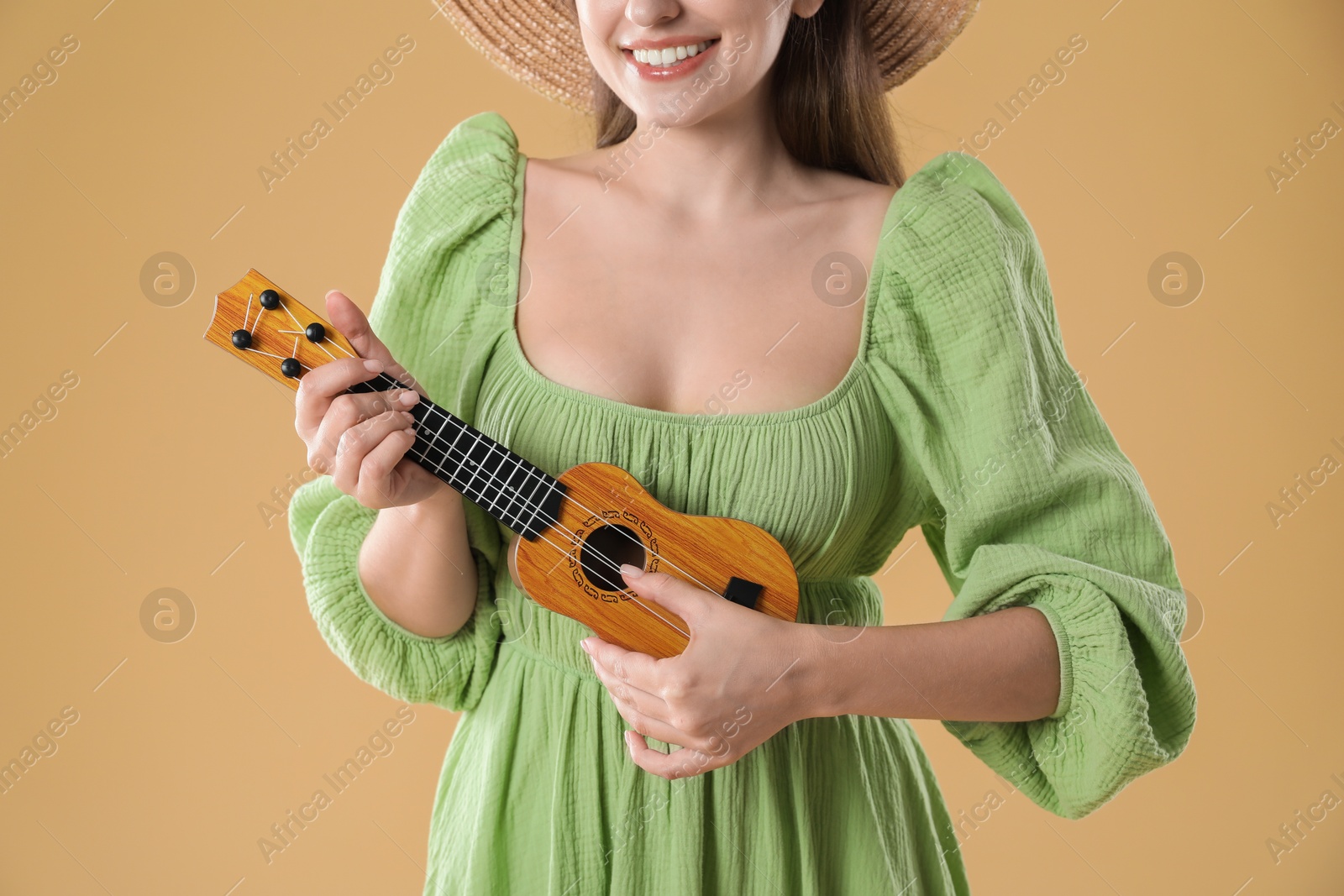 Photo of Woman playing ukulele on beige background, closeup