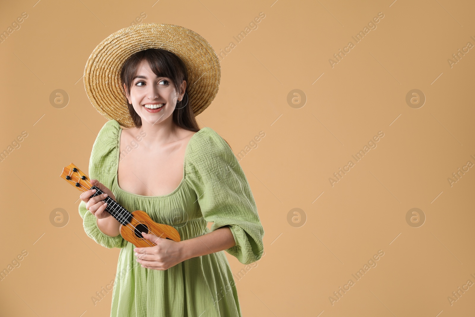 Photo of Happy woman playing ukulele on beige background, space for text