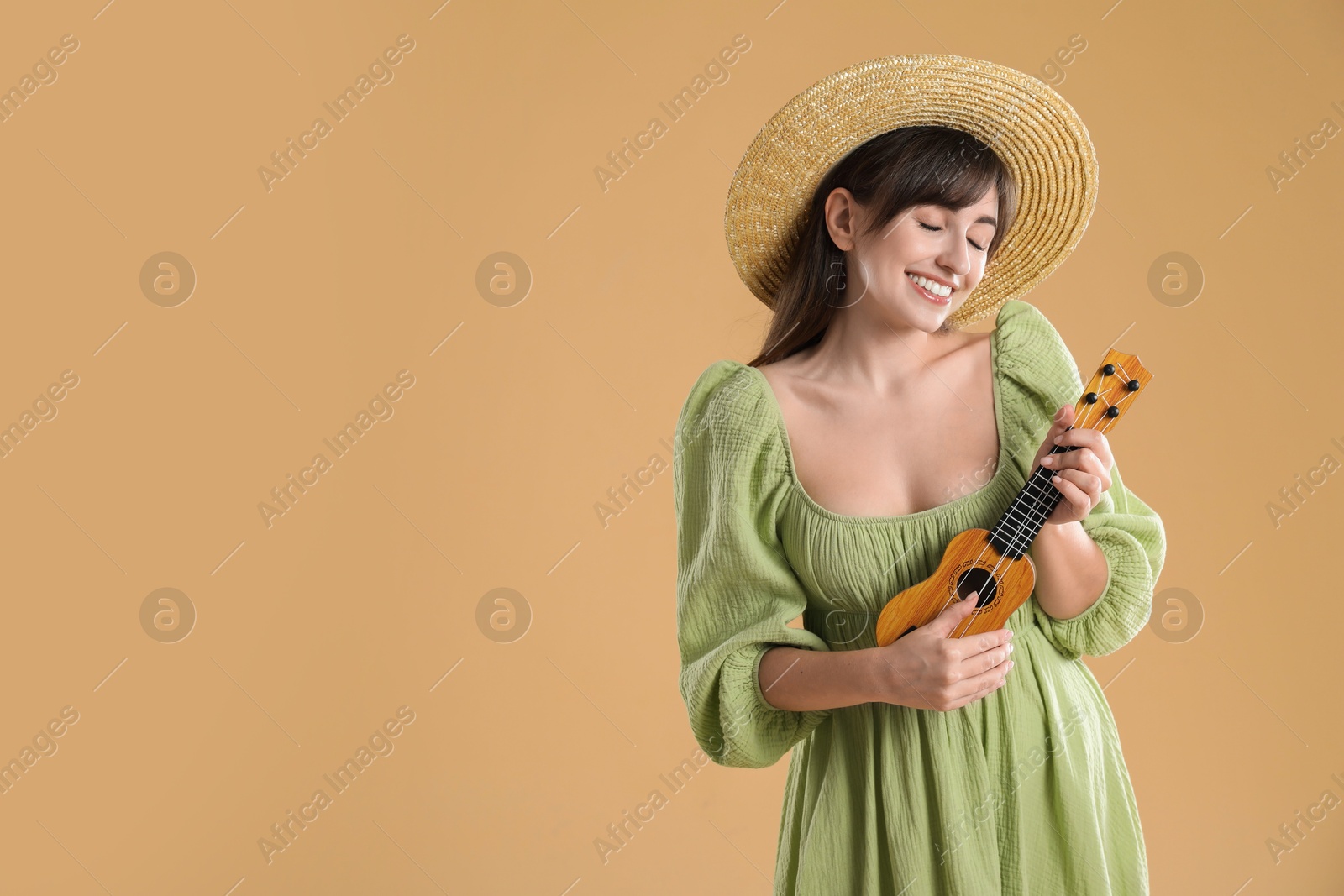 Photo of Happy woman playing ukulele on beige background, space for text