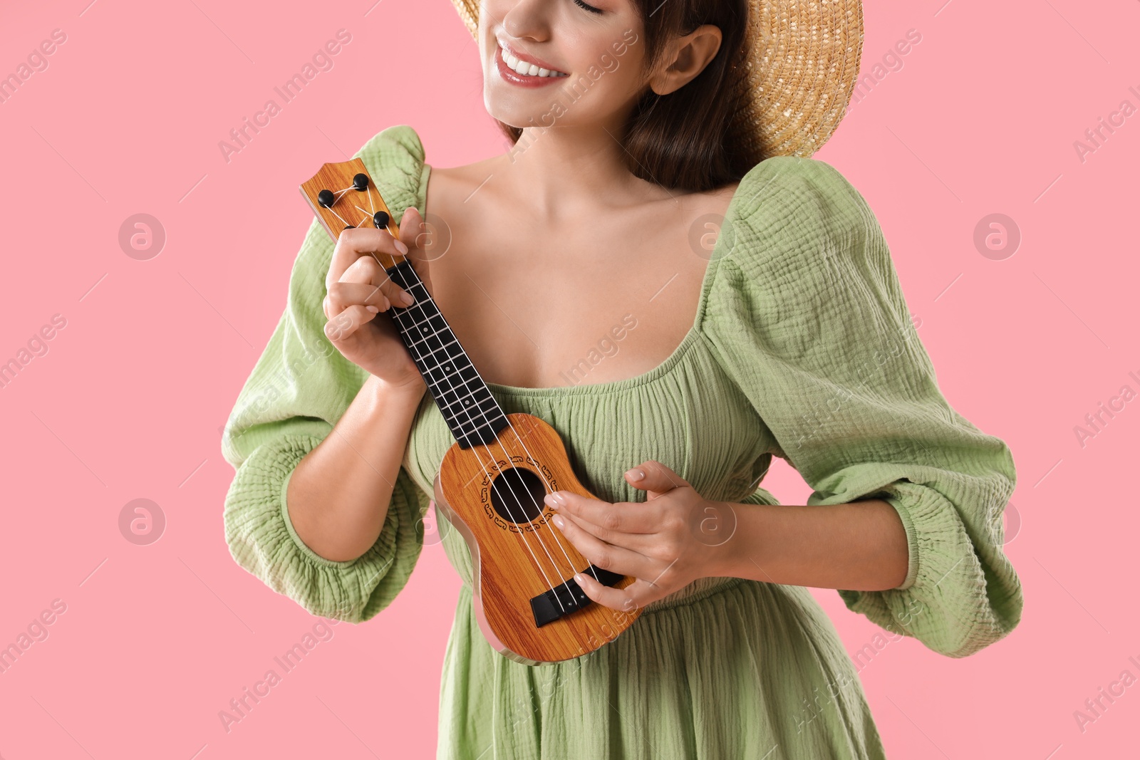 Photo of Woman playing ukulele on pink background, closeup