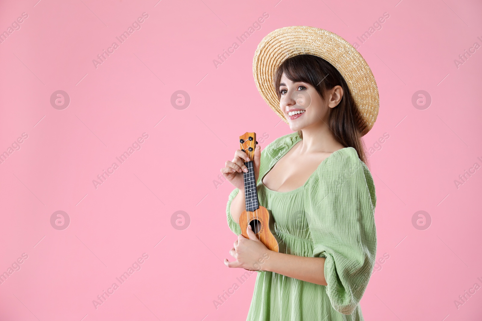 Photo of Happy woman playing ukulele on pink background, space for text