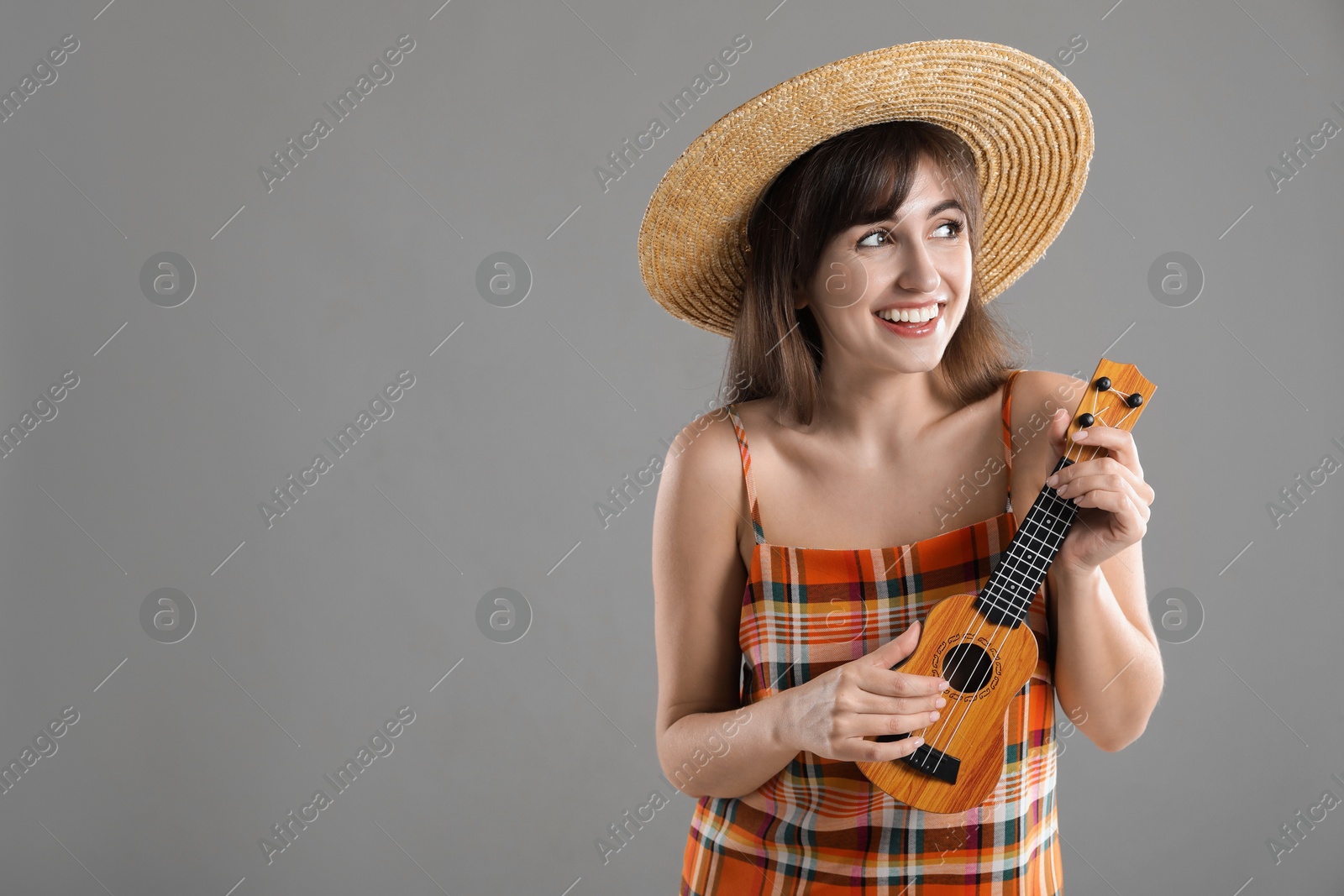 Photo of Happy woman playing ukulele on grey background, space for text