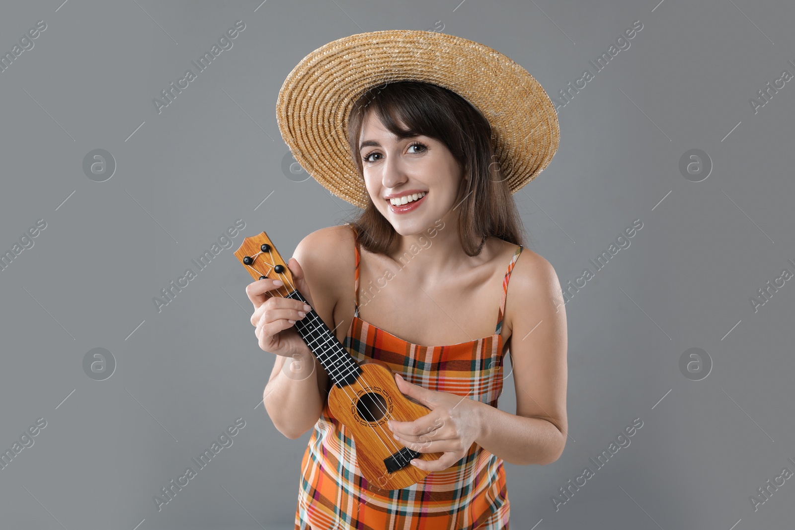 Photo of Happy woman playing ukulele on grey background