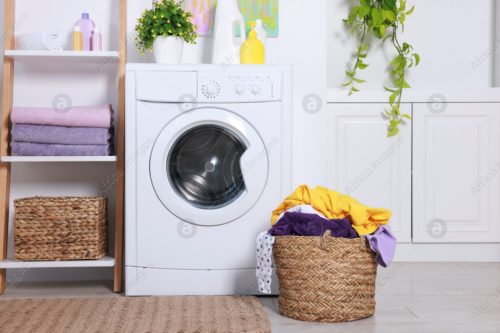 Photo of Washing machine, detergents, clean towels and basket with laundry in room