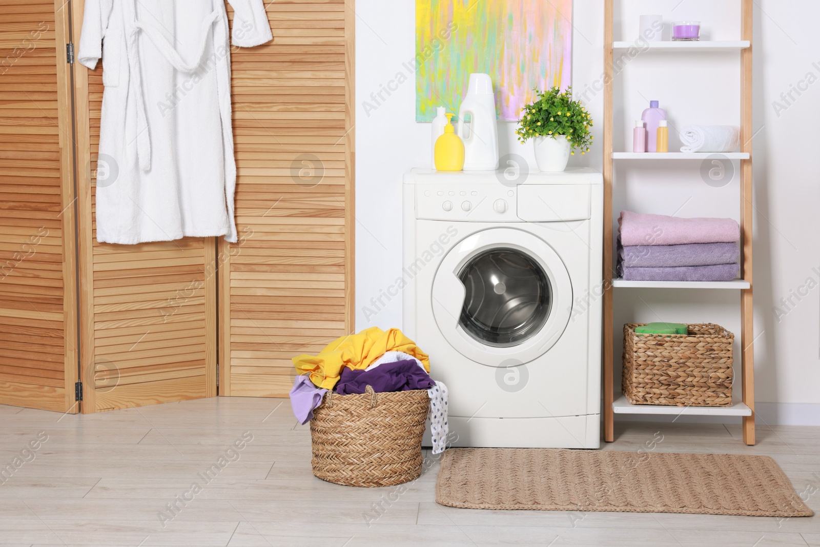 Photo of Washing machine, detergents, clean towels and basket with laundry in room